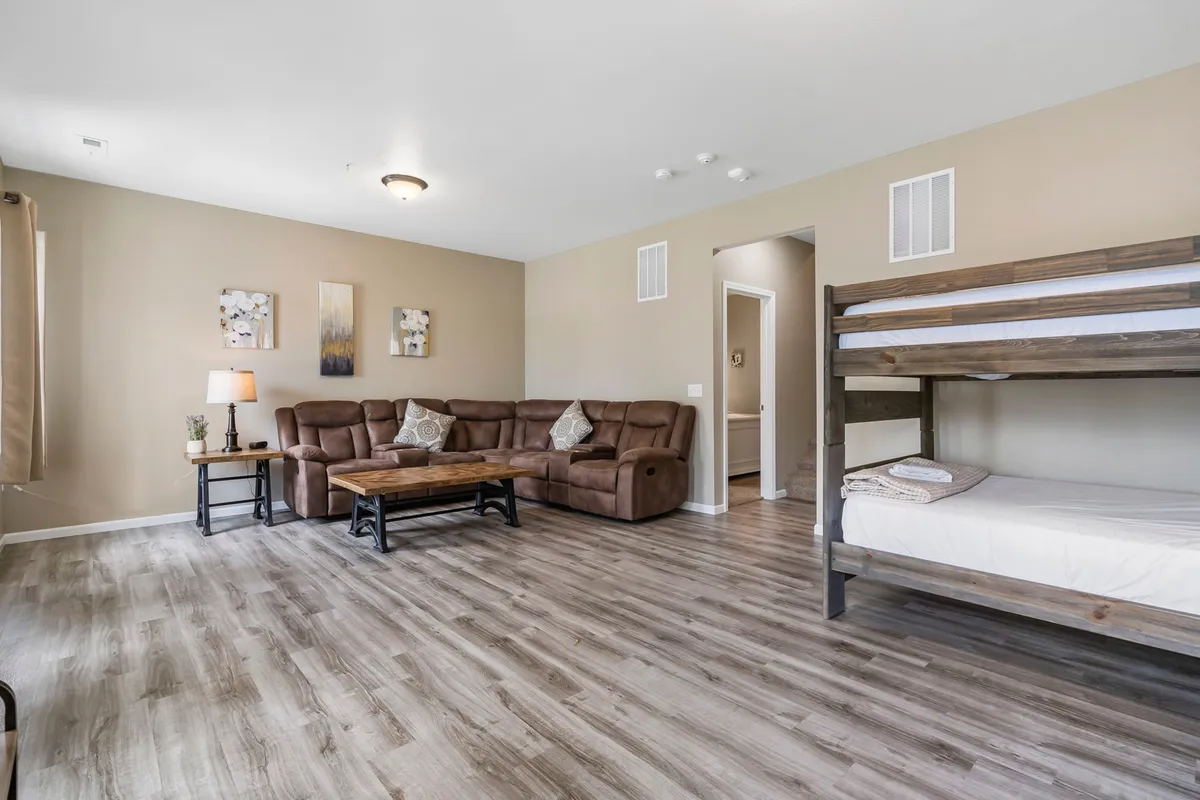 A cozy living area featuring a leather sofa, wooden coffee table, and a bunk bed in the background. The setup underlines the dual-purpose design of the space for both relaxation and extra sleeping accommodations.