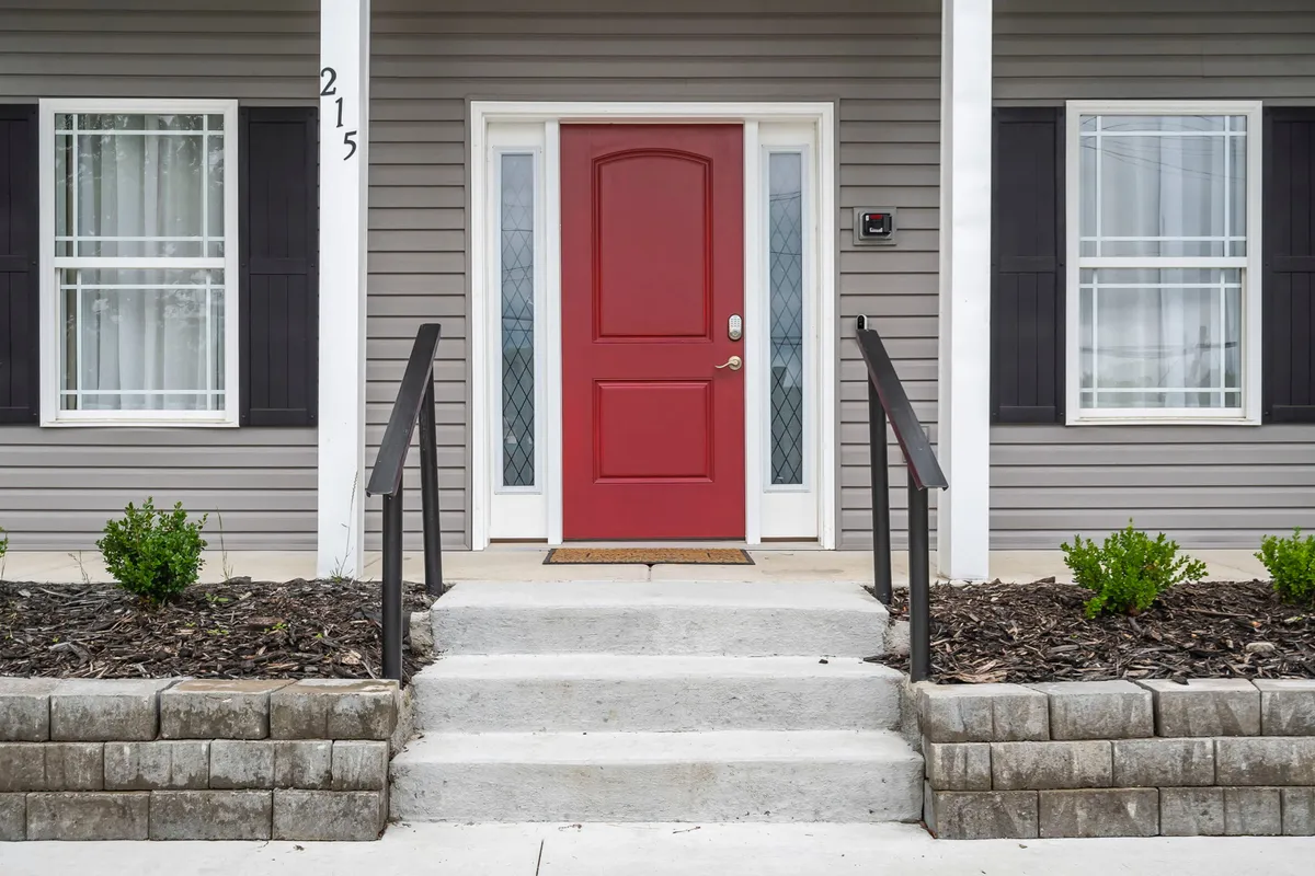 The image captures the red front door of Third Street Retreat, with steps leading up to the entrance and a neatly landscaped area featuring small plants. The inviting entryway sets the tone for arriving guests and hints at a welcoming atmosphere for group gatherings.