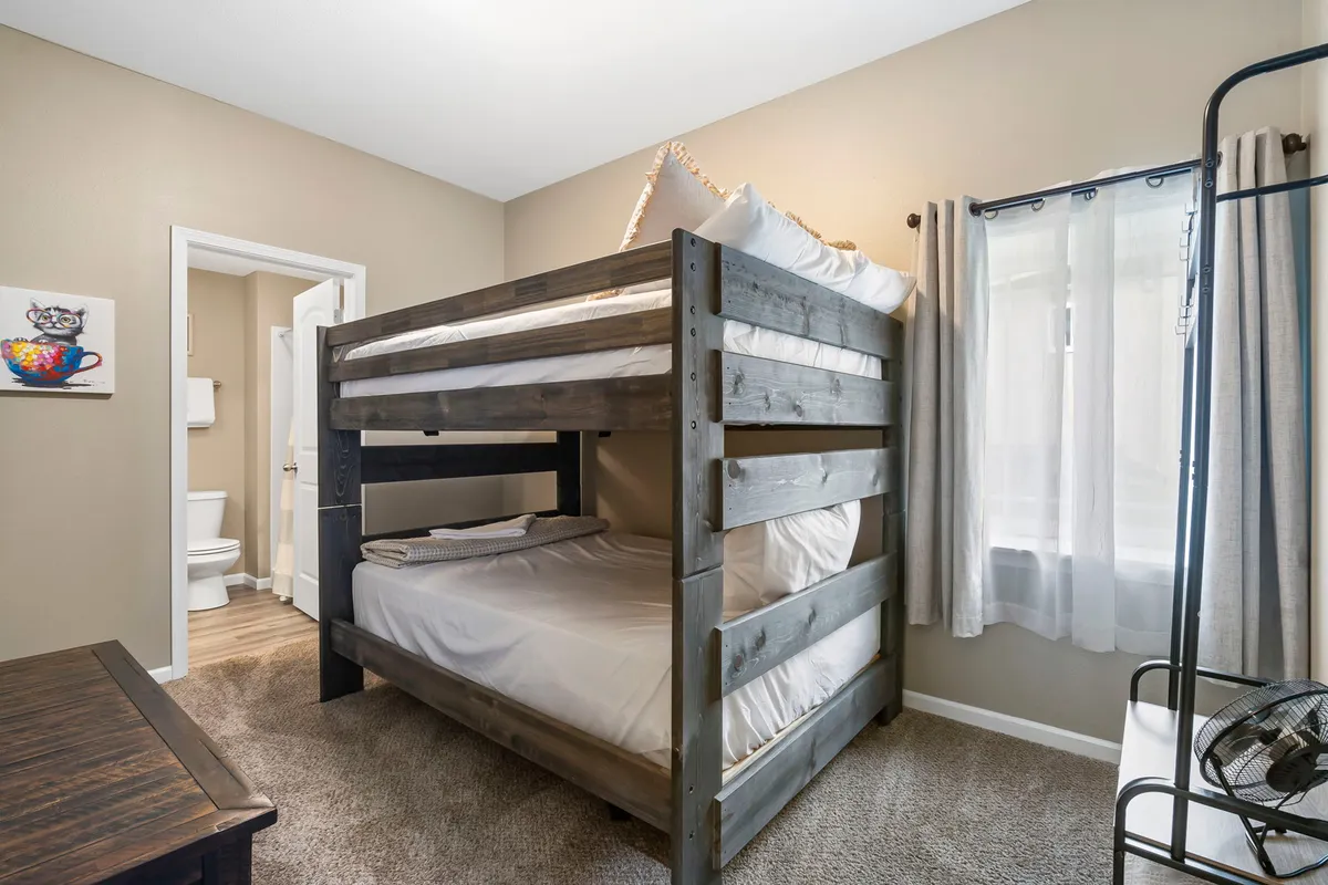 A bright and inviting bunk room with a full-over-full bunk bed, a window letting in natural light, and playful artwork adorning the wall. The space feels both fun and functional, perfect for kids or groups.