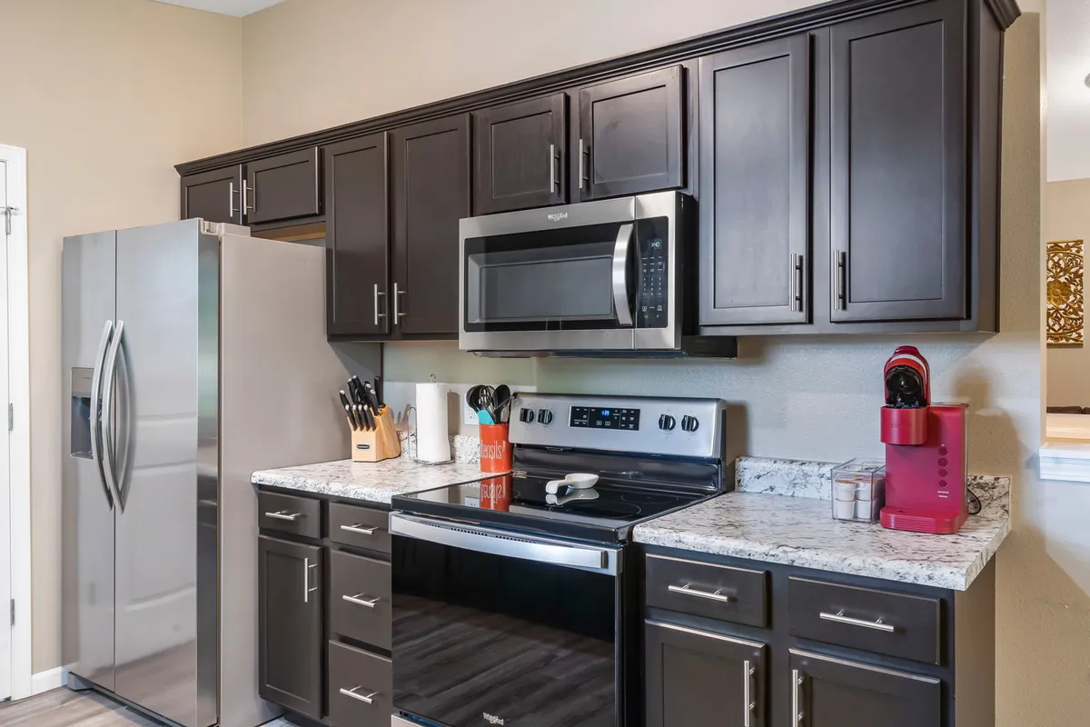 A detailed look at the kitchen, showcasing stainless steel appliances including a refrigerator and microwave, granite countertops, and ample cabinetry. The setup is clean and modern, evoking a sense of readiness for meal prep, baking, or entertaining guests.