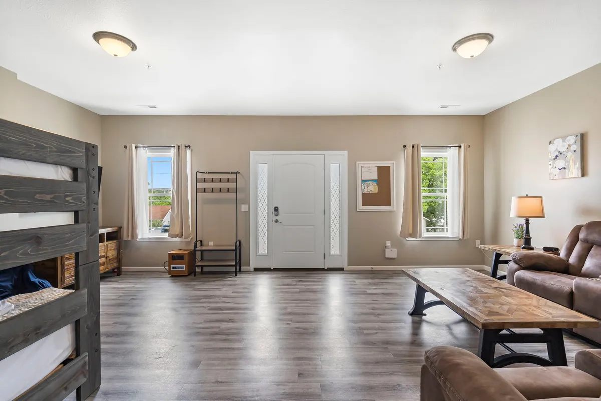 This image features the front door of the property, visible within an inviting living area that includes a sofa, coffee table, and windows letting in natural light. The space is styled for gathering and relaxation, hinting at easy access to the neighborhood and a welcoming return after exploring downtown Branson.