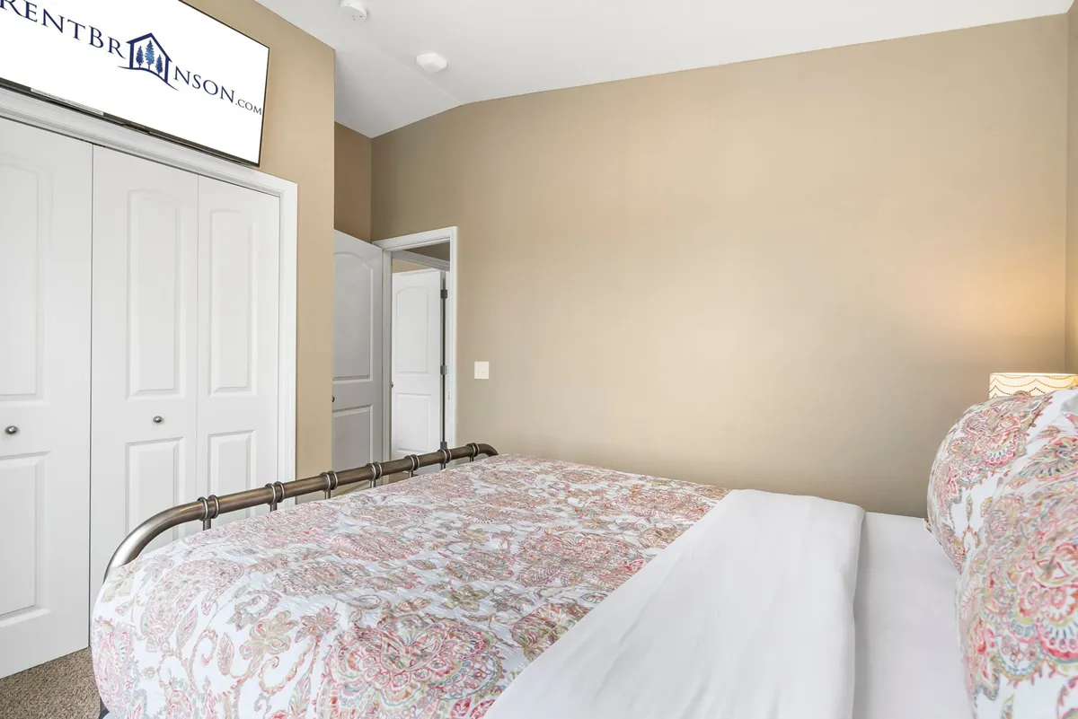 A serene bedroom with a plush bed featuring patterned bedding, a wall-mounted TV, and closet doors. The room is softly lit, radiating a relaxing and welcoming atmosphere ideal for unwinding after a day of adventure.