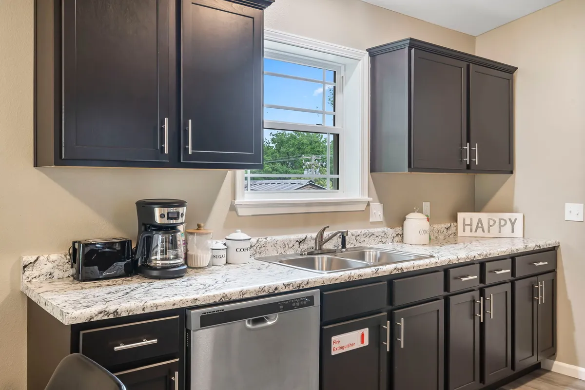 The kitchen scene showcases black cabinets, a granite countertop, a coffee maker, and a bright window. The cheerful mood and breakfast setup hint at mornings spent preparing coffee or meals before heading out for the day.